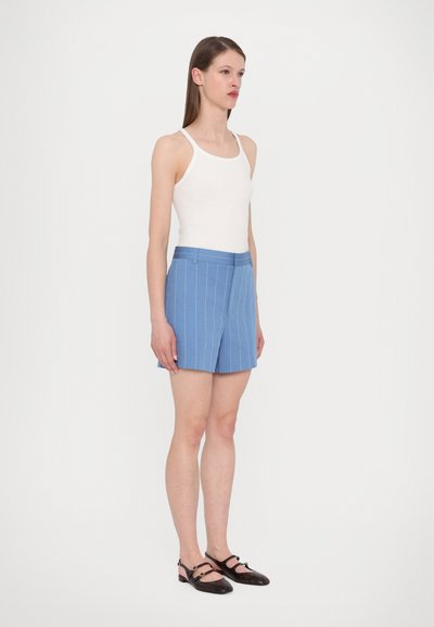 Blå stribede shorts med flad front, sidelommer og glat tekstur. Kombination med en hvid tanktop og sorte sandaler.