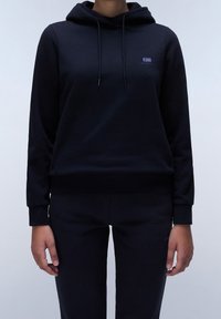 Sudadera negra ajustada con un ajuste ceñido, que cuenta con un bolsillo delantero, cordones ajustables y un pequeño logo en el pecho. Textura de tela suave.