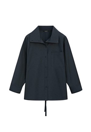 Chemise boutonnée à manches longues de couleur bleu marine foncé, avec un large col, une poche poitrine unique, des manches avec poignets retroussés, et un lien en tissu suspendu à l'ourlet.