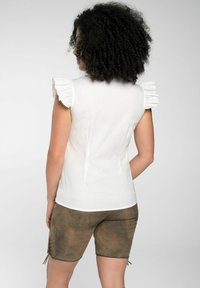 Weißes ärmelloses Oberteil mit Rüschendetails an den Schultern; glatter Stoff. Kombiniert mit braunen, strukturierten Shorts mit Schnürdetails an den Seiten.