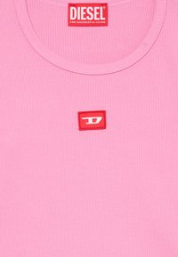 Débardeur rose à côtes avec un col rond et un petit patch logo rectangulaire rouge avec des lettres blanches sur le côté gauche.