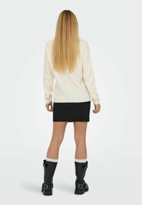 Cremfarbener Strickpullover, schwarzer Wildleder-Minirock und schwarze kniehohe Stiefel mit Schnallen und weißen Akzenten, von hinten betrachtet.