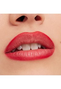 Gros plan de lèvres avec du rouge à lèvres rouge légèrement entrouvertes, montrant les dents de devant supérieures et une partie du nez au-dessus.