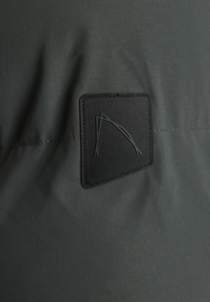 Zwarte stoffen patch met een verhoogd abstract ontwerp op een gladde, donkergrijze textielachtergrond, die een gedempte kleurenpalet en een strakke textuur laat zien.