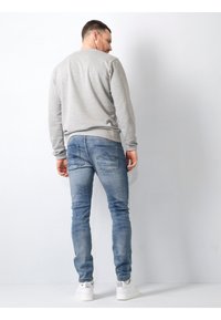 Hanorac gri cu guler rotund, blugi slim-fit albaștri cu buzunare la spate și adidași albi, evidențiind o ținută casual, relaxată din spate.