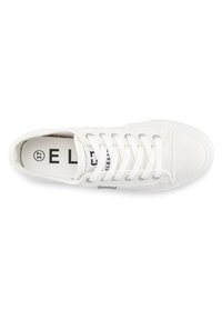 White canvas sneaker with round toe, silver eyelets, and flat white laces. Textured sole detail and printed logo on the insole.