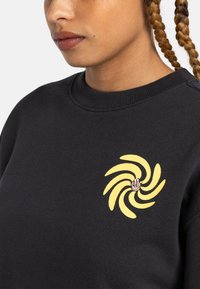 Black sweatshirt featuring a yellow swirl design with a central red and white accent. Ribbed neckline and textured fabric.