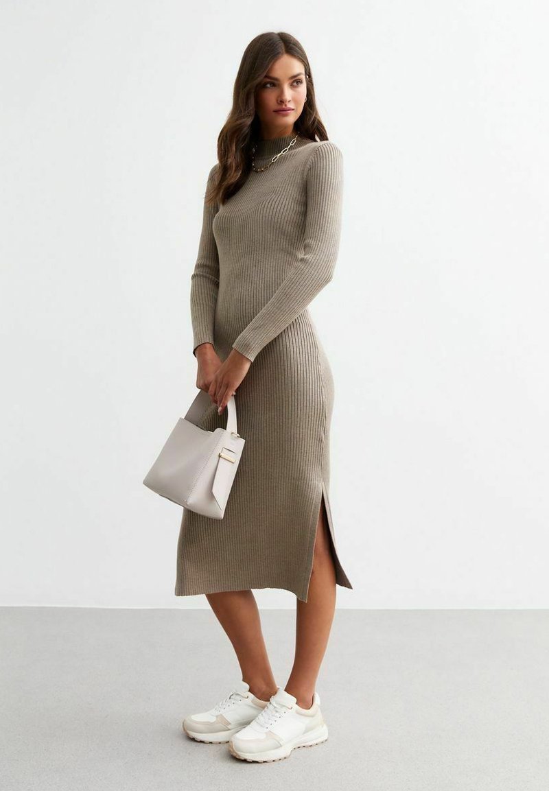 Abito in maglia a coste, maniche lunghe, color taupe, con spacco laterale, abbinato a scarpe da ginnastica bianche e una piccola borsa beige strutturata.