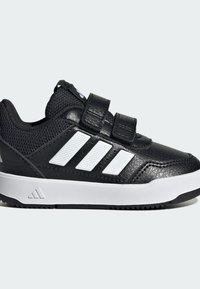 Crna sportska cipela s gornjim dijelom od sintetičkog materijala, bijelim prugastim detaljima, trakama na čičak i teksturiranom površinom. Ima gumu na potplatu za bolje prianjanje.