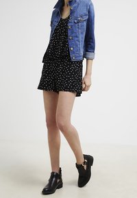 Veste en denim avec des boutons en métal, un haut noir à pois, un short assorti et des bottines noires avec des ouvertures et des accents de boucles.