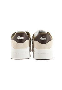 Sneakers Lacoste con parte superiore in suede beige, dettagli in pelle marrone e suole bianche. Logo presente sul tallone, design arrotondato.