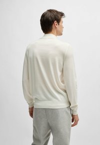 Light cream pullover with long sleeves, made of soft material. Features a ribbed hem and collar, paired with light gray sweatpants.