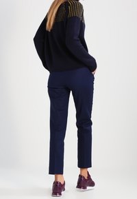 Maglione navy con un motivo testurizzato giallo e nero nel corpetto, abbinato a pantaloni navy e sneakers borgogna con suole bianche.