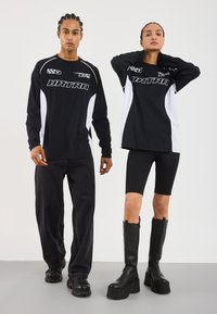 Black long-sleeve shirts with white accents, paired with dark jeans and black high-heeled boots. Features bold logos and sporty design.