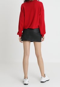 Maglione oversize rosso, gonna mini nera, sneakers bianche. Tessuto morbido, vestibilità rilassata, design essenziale, con una superficie liscia e senza motivi visibili.