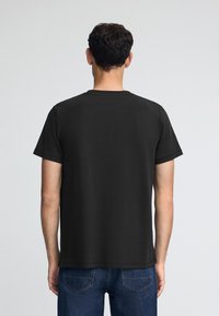 Zwarte katoenen t-shirt met een klassieke ronde halslijn en korte mouwen, met een zachte textuur en rechte zoom. Gedragen met blauwe jeans.