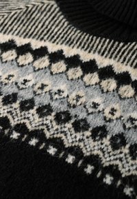 Schwarzer Strickpullover mit einem gemusterten Schulterbereich in Grau, Creme und Schwarz. Beinhaltet geometrische und florale Motive sowie einen gerippten Halsauschnitt.