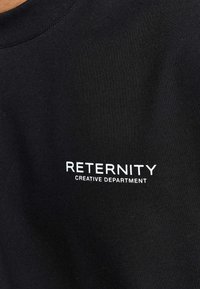 T-shirt nera in cotone con testo bianco che recita "RETERNITY CREATIVE DEPARTMENT." Semplice collo rotondo, texture morbida, design aderente.