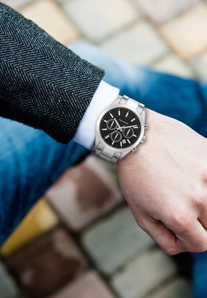 Silberner Metallarmbanduhr mit einem runden schwarzen Zifferblatt, drei Teilzifferblättern und einer Datumsanzeige. Verfügt über ein poliertes Finish und ein Gliederarmbanddesign.