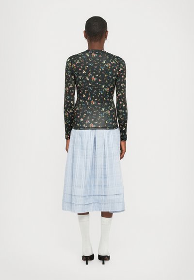 Tricou negru cu mânecă lungă și imprimeu floral, asortat cu o fustă plisată bleu deschis. Modelul poartă șosete albe și pantofi cu toc negri.