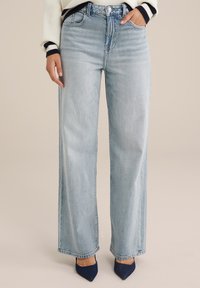Jeans de pierna ancha en azul claro con una cintura alta, con cinco bolsillos y un acabado desgastado. La tela tiene una apariencia suave y ligeramente texturizada.