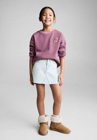 Lila randig långärmad sweatshirt med logotyp, ljusblå denim A-linje kjol och bruna fårskinnsstövlar med pälskanter.