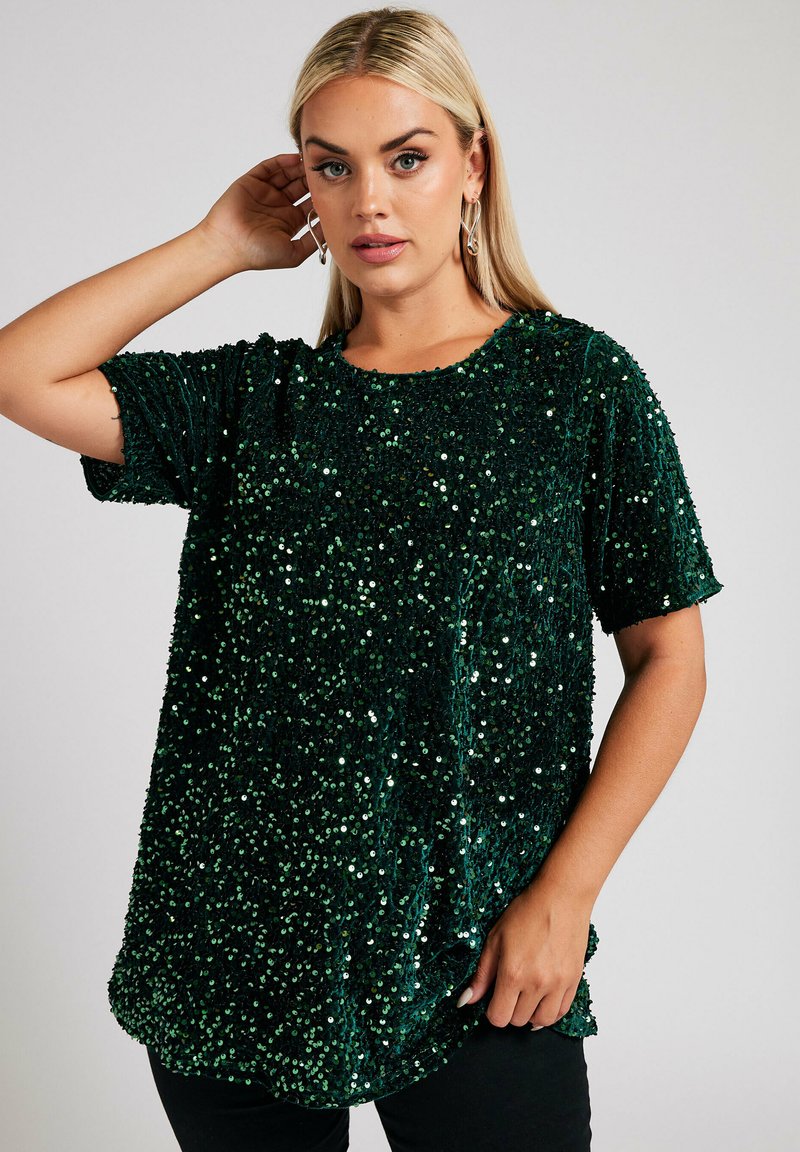 Top corto verde con paillettes, maniche corte e scollatura rotonda, dalla consistenza lucida e una vestibilità morbida. L'orlo presenta una leggera curvatura nella parte inferiore.