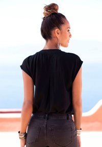 Schwarzes T-Shirt mit kurzen Ärmeln, locker geschnitten und mit einem subtilen Rückennaht-Detail, kombiniert mit dunklen Jeans.