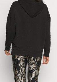 Felpa nera oversized con cappuccio, caratterizzata da polsini e orlo a coste. Abbinata a leggings con un motivo astratto nero e oro.