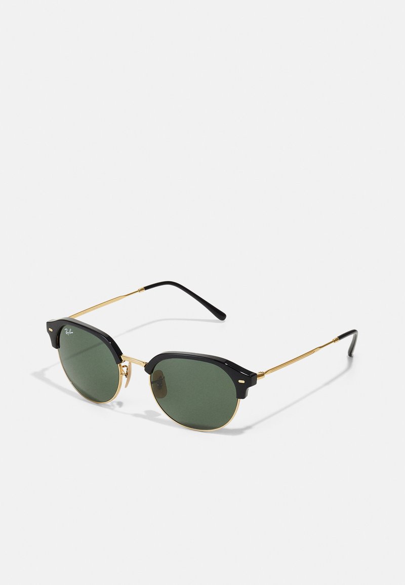 Gafas de sol negras y doradas con lentes verdes redondos, que presentan un diseño de cejilla único y brazos delgados dorados con puntas negras.