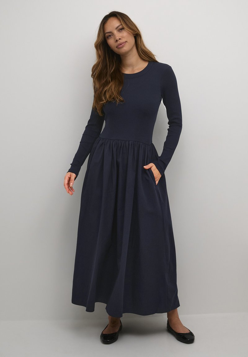 Navy long-sleeve dress with a fitted ribbed bodice and a flowing, gathered skirt. Features side pockets and smooth texture.