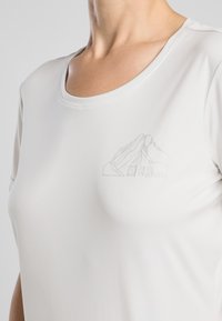 Camiseta grigio chiaro a maniche corte realizzata in un tessuto morbido. Presenta un sottile contorno di montagna e un logo sulla zona del petto. Design con colletto rotondo.