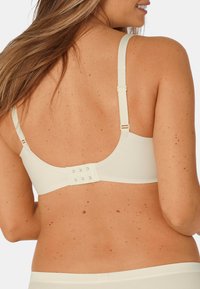 Krémová podprsenka s nastavitelnými ramínky, hladkým povrchem a zapínáním na háček a oko na zadní straně. Vyznačuje se minimalistickým designem a jednoduchou konstrukcí.