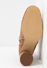 Chaussure en cuir tressé marron présentée semelle vers le haut, montrant un talon en caoutchouc texturé et la marque de taille 37 sur la semelle beige lisse.