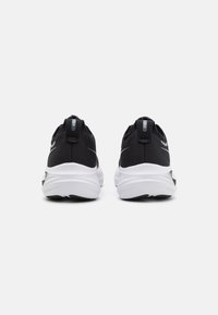 Scarpe da ginnastica nere con tomaia in rete, suole bianche e dettagli riflettenti; progettate con tacchi imbottiti e un motivo nero testurizzato.