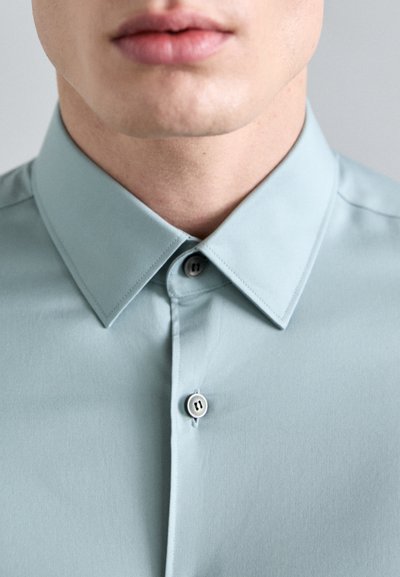 Camisa de color azul claro con cuello, que presenta una textura suave, dos botones en el cuello y detalles de costura precisos en el cuello y la tapeta.