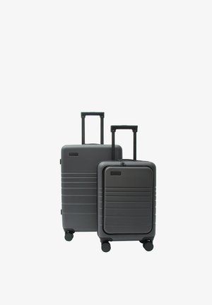 Dwie czarne, twarde walizki różnej wielkości z wysuniętymi teleskopowymi uchwytami i czterema obrotowymi kółkami na białym tle.