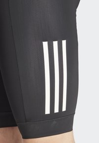 Pantaloni shorts sportivi neri realizzati in materiale liscio ed elastico, con tre strisce bianche verticali sulla coscia sinistra e una vita strutturata.