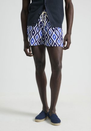 Bañador azul con estampado y formas de diamante en blanco, con cintura elástica y cordón ajustable, combinado con espadrilles marinos, sobre un fondo neutro.