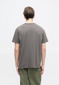 Camiseta de algodón gris con un corte relajado, cuello redondo y mangas cortas, combinada con pantalones cargo verdes oliva. Diseño minimalista.