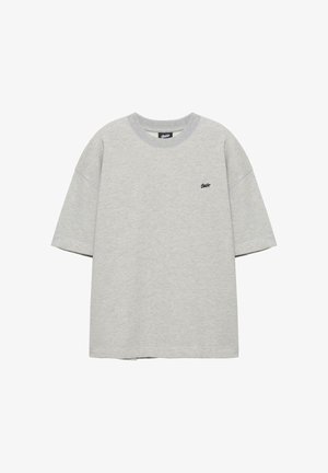 Hellgraues T-Shirt mit kurzen Ärmeln und Rundhalsausschnitt, mit kleinem schwarzem Logo auf der linken Brust, flach auf weißem Hintergrund präsentiert.