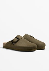 Mockasiner i olivgrönt av mocka med en formad fotbädd, öppen baksida och en matt svart spänne. Texturerad yta och gummisula.