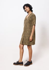 Robe courte à motif léopard en tissu léger, dotée d'un décolleté en V et de manches courtes. Assortie à des chaussures noires à lacets avec une épaisse semelle.