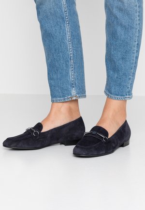 Marineblå ruskinds loafers med flad hæl og sølvfarvede hardwaredetaljer. Rund tå og glat tekstur, parret med lyseblå denim.