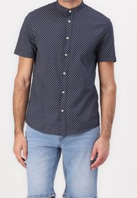 Camisa de manga corta en azul marino oscuro con un pequeño patrón geométrico blanco, con cuello mao y botones de color claro.