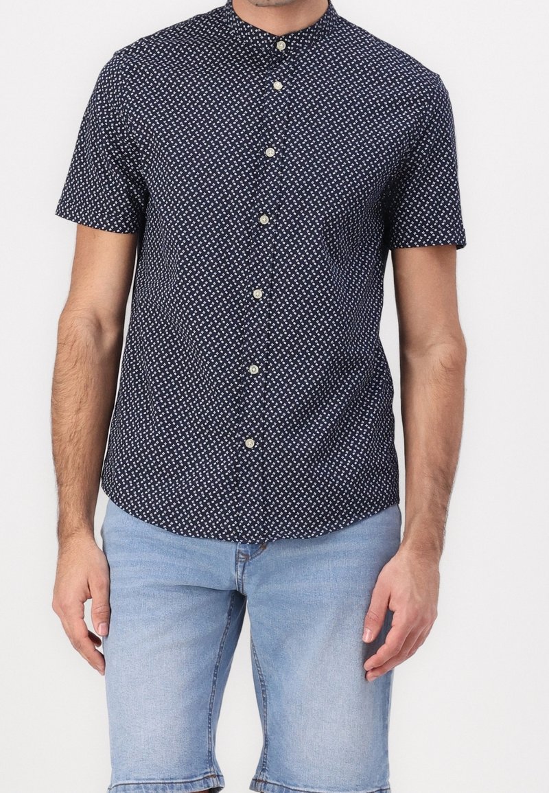 Camicia a maniche corte in blu navy scuro con un piccolo motivo geometrico bianco, caratterizzata da un colletto alla coreana e bottoni di colore chiaro.