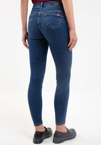 Jeans ajustados de tela vaquera azul oscuro, con una cintura de altura media y un diseño clásico de cinco bolsillos, con un pequeño logo en el bolsillo trasero.