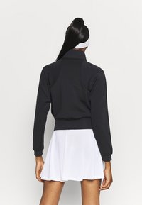 Sudadera negra recortada con cuello alto y mangas largas, combinada con una falda blanca acampanada. Tejido liso y detalles mínimos.