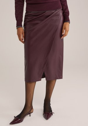 Fustă din piele burgundy, cu un tiv până la genunchi și o deschidere laterală, asortată cu colanți negri transparenți și pantofi cu toc slingback cu vârful ascuțit.