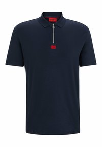 Námořnická modrá polo košile z jemné bavlny s límečkem na zip, která má na přední straně malou červenou značku a krátké rukávy.